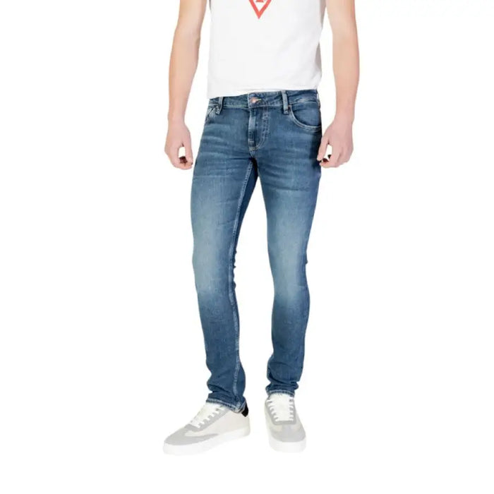 Man in Guess Men Distressed Blue Jeans paired with white sneakers