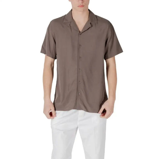 Man wearing a brown short-sleeved button-down shirt and white pants