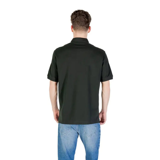 Man wearing dark green polo shirt with white shoulder stripe and blue jeans