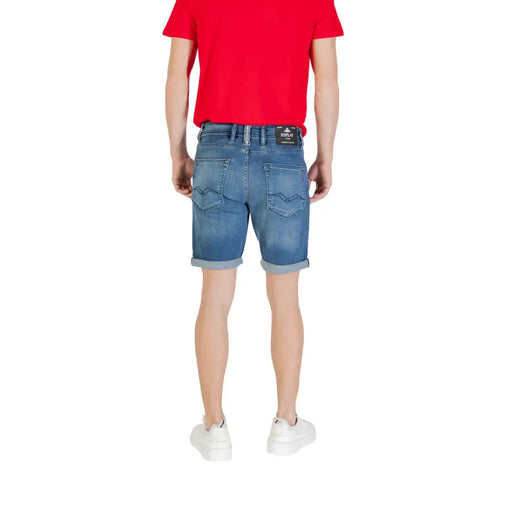 Man wearing denim shorts, white sneakers, and a red T-shirt in a product display