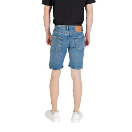 Man wearing denim shorts and white sneakers in a casual outdoor setting