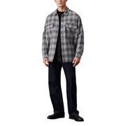 Man in gray plaid Calvin Klein Jeans button shirt, black t-shirt, and dark jeans