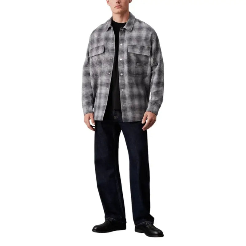 Man in gray plaid Calvin Klein Jeans button shirt, black t-shirt, and dark jeans