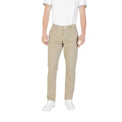 Un homme porte un pantalon beige à fermeture éclair et bouton, associé à des baskets blanches.