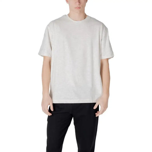 Man wearing a light-colored T-shirt and black pants standing confidently