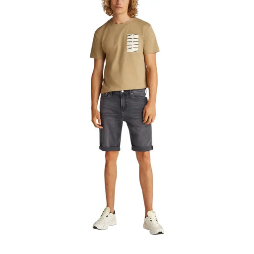 Man wearing a tan T-shirt and gray denim shorts, suitable for casual summer wear