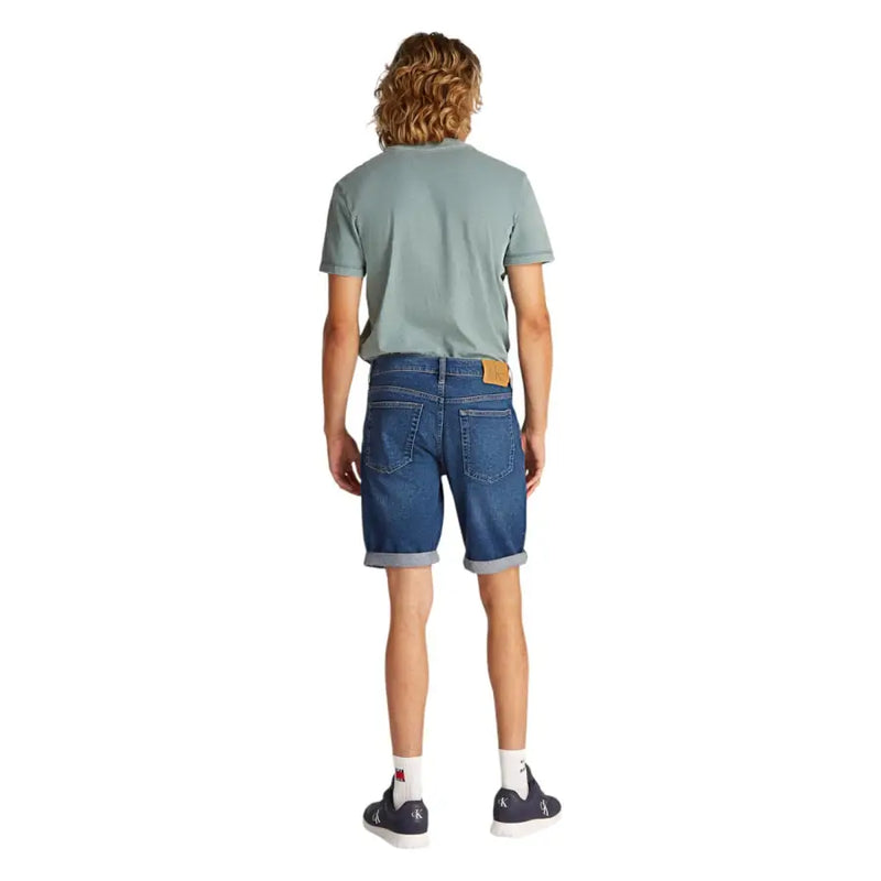 Mens blue denim shorts shown from the back with rolled cuffs and a tan leather brand patch on the waistband