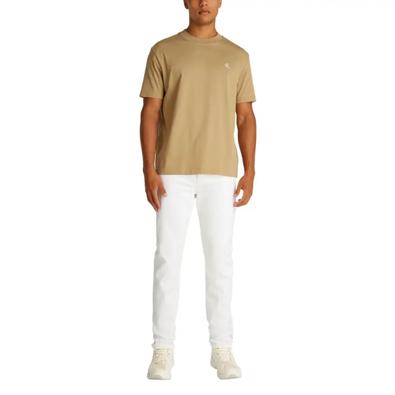 Men’s white denim jeans paired with a beige short-sleeved crew neck t-shirt featuring a small white embroidered logo