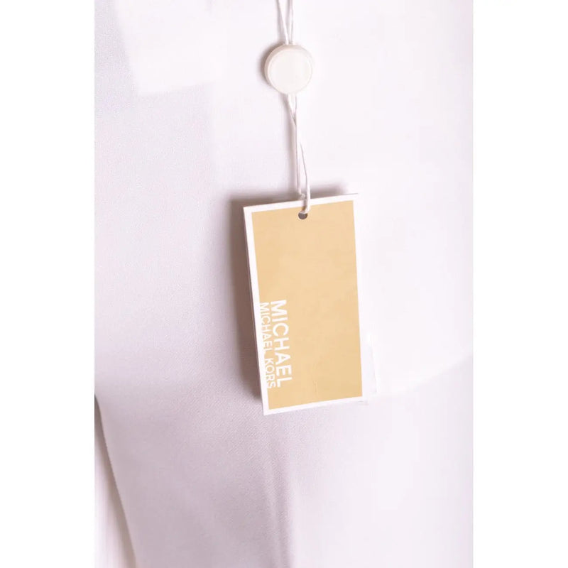Une étiquette beige de la marque Michael Kors avec des lettres blanches est attachée à un pantalon blanc stretch pour femme à fermeture éclair et boutons.