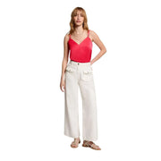 Une femme porte un Morgan De Toi Débardeur en satin corail à col en V et fines bretelles, porté avec un pantalon blanc à jambes larges.