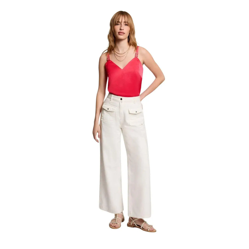 Une femme porte un Morgan De Toi Débardeur en satin corail à col en V et fines bretelles, porté avec un pantalon blanc à jambes larges.