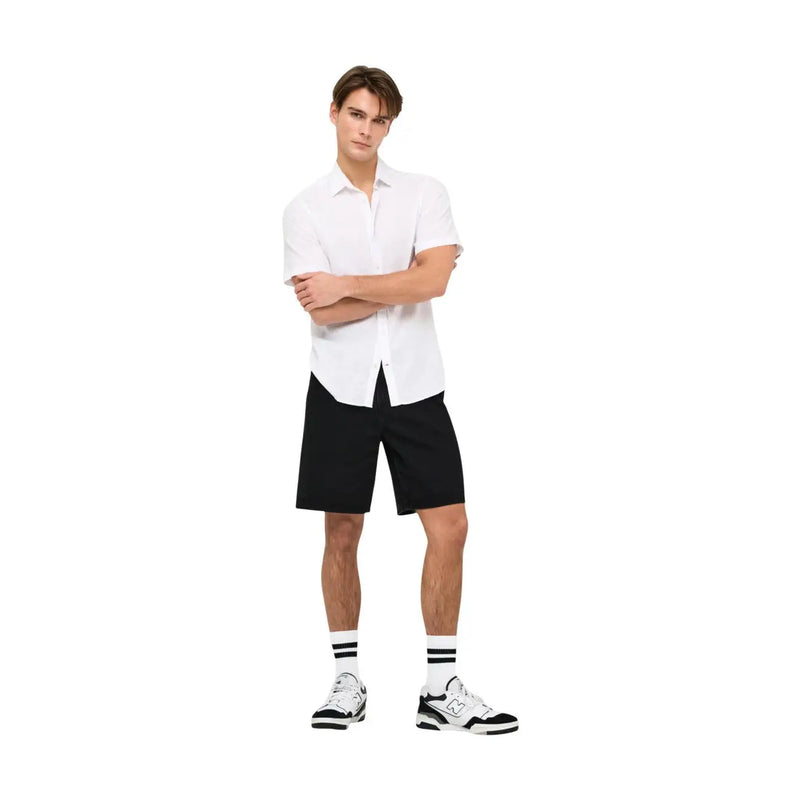 Only Short en jean noir délavé pour homme, porté par un mannequin (vue de face), associé à une chemise blanche à manches courtes et des baskets.