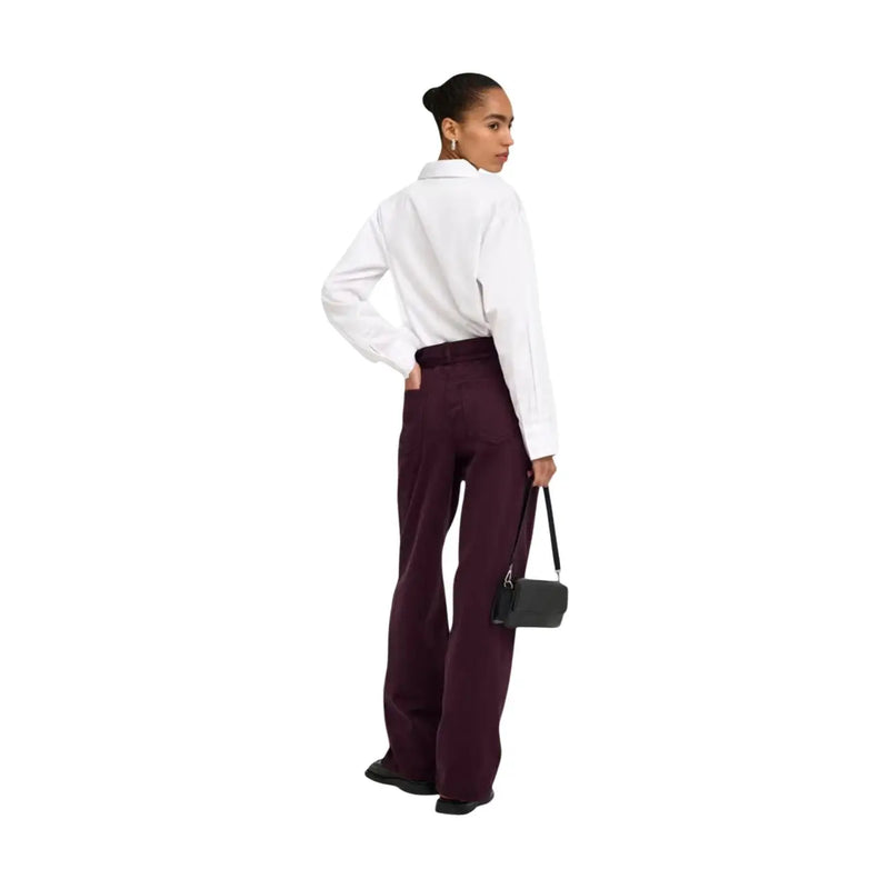Un élégant mini sac bandoulière en cuir noir, au design minimaliste et à la fine bandoulière, s'accorde parfaitement avec un jean violet en coton à ceinture.