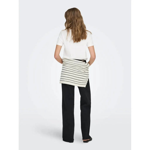 Un t-shirt court blanc en coton à col rond, porté avec une jupe portefeuille en maille côtelée rayée blanche et noire sur un pantalon foncé.
