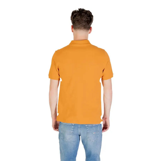 Person wearing a mustard colored short sleeve polo shirt and blue jeans
