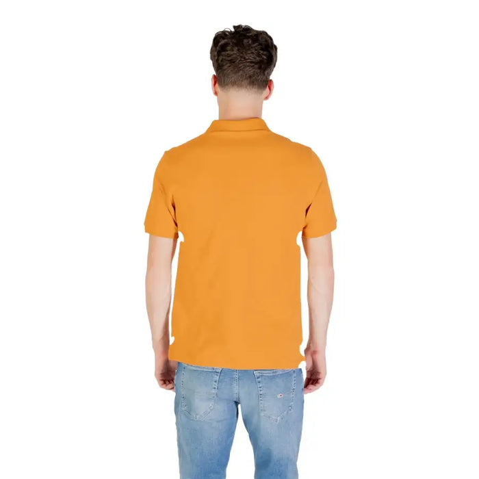 Person wearing a mustard colored short sleeve polo shirt and blue jeans