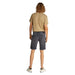 Man wearing a tan T-shirt and gray denim shorts posing outdoors