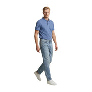 Un homme portant un jean Replay bleu clair coupe slim en coton stretch et un polo bleu clair, debout de face.