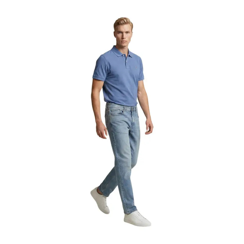 Un homme portant un jean Replay bleu clair coupe slim en coton stretch et un polo bleu clair, debout de face.