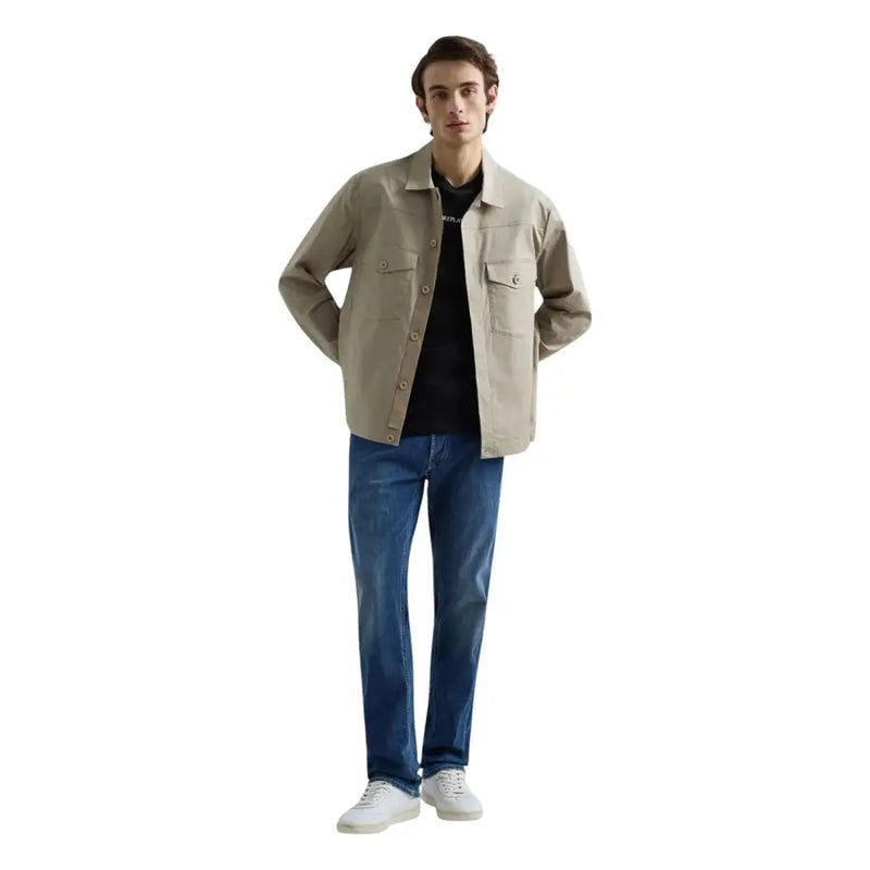 Veste utilitaire beige à boutons et deux poches poitrine, portée avec un jean droit bleu stretch pour homme de la marque Replay.