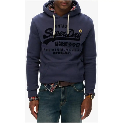 Navy blue Superdry men’s printed hooded sweatshirt with front pockets worn over plaid shirt and jeans