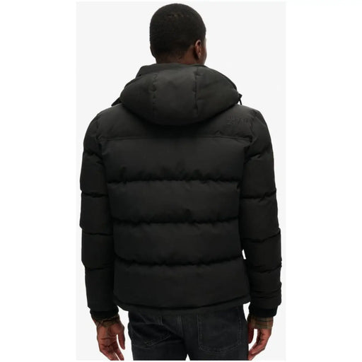 Superdry Doudoune longue noire à capuche pour homme, avec empiècements matelassés, conçue pour les conditions hivernales.