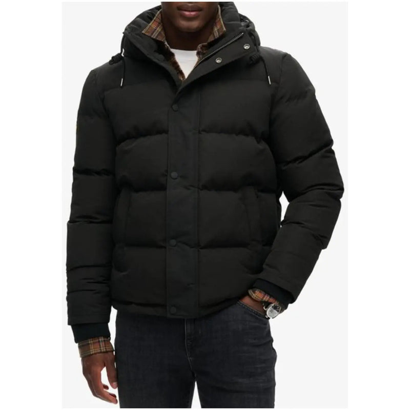 Superdry Doudoune longue noire à capuche pour homme, style hivernal, avec capuche doublée à carreaux, fermeture boutonnée et design matelassé.