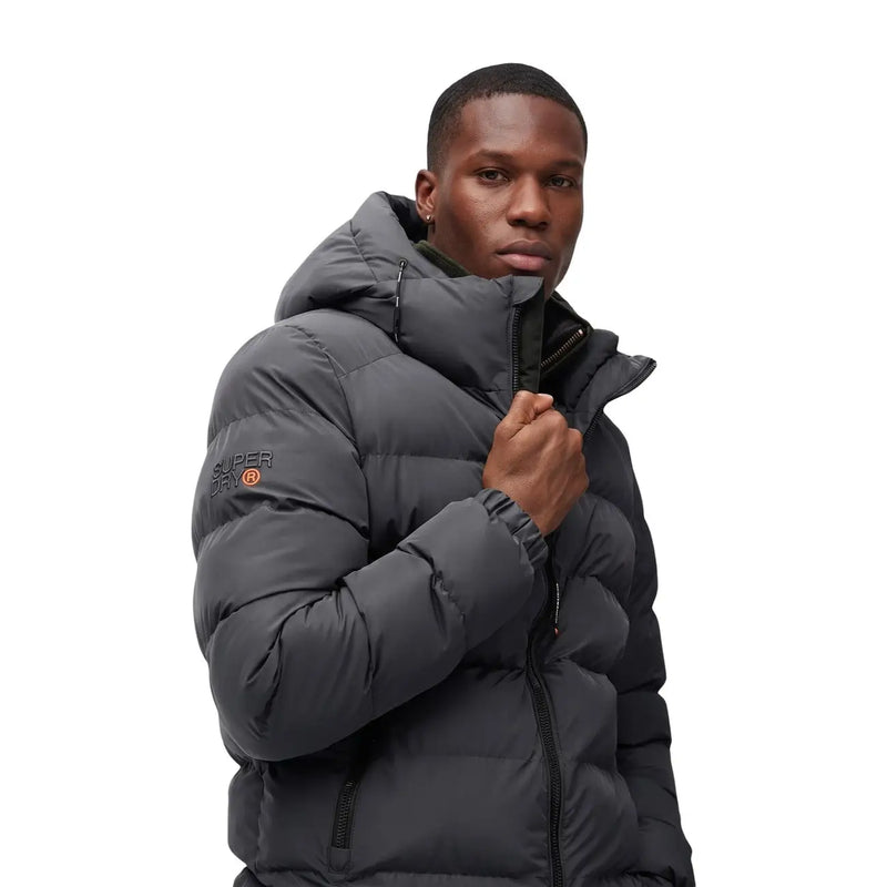 Superdry Doudoune homme gris foncé à capuche, matelassée, avec logo sur la manche gauche (vue de face).