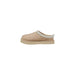 Tan UGG slipper with slip-on design and decorative trim for casual comfort