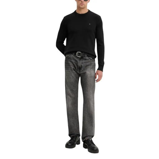 Black crew neck sweater with a small logo on the chest, dark wash straight-leg jeans with belt loops and button fly.