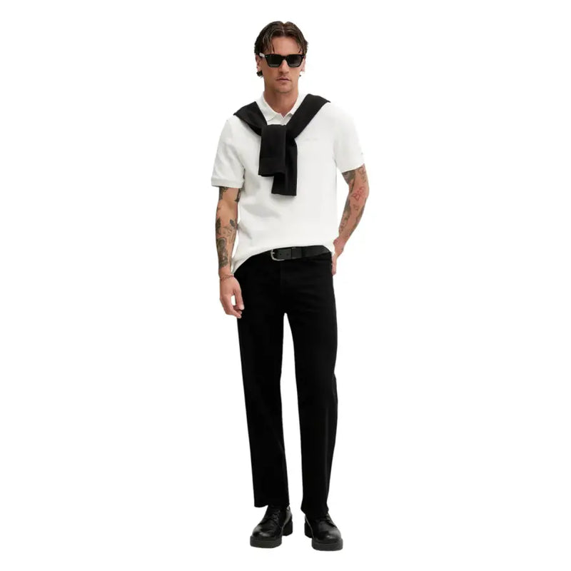 Un homme portant un polo blanc à manches courtes et une cravate noire, ainsi qu'un pull en maille de coton noir Tommy Hilfiger Jeans.