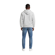 A man wearing a grey organic cotton hoodie and blue denim jeans from Tommy Hilfiger Jeans men collection