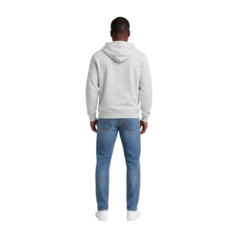 A man wearing a grey organic cotton hoodie and blue denim jeans from Tommy Hilfiger Jeans men collection