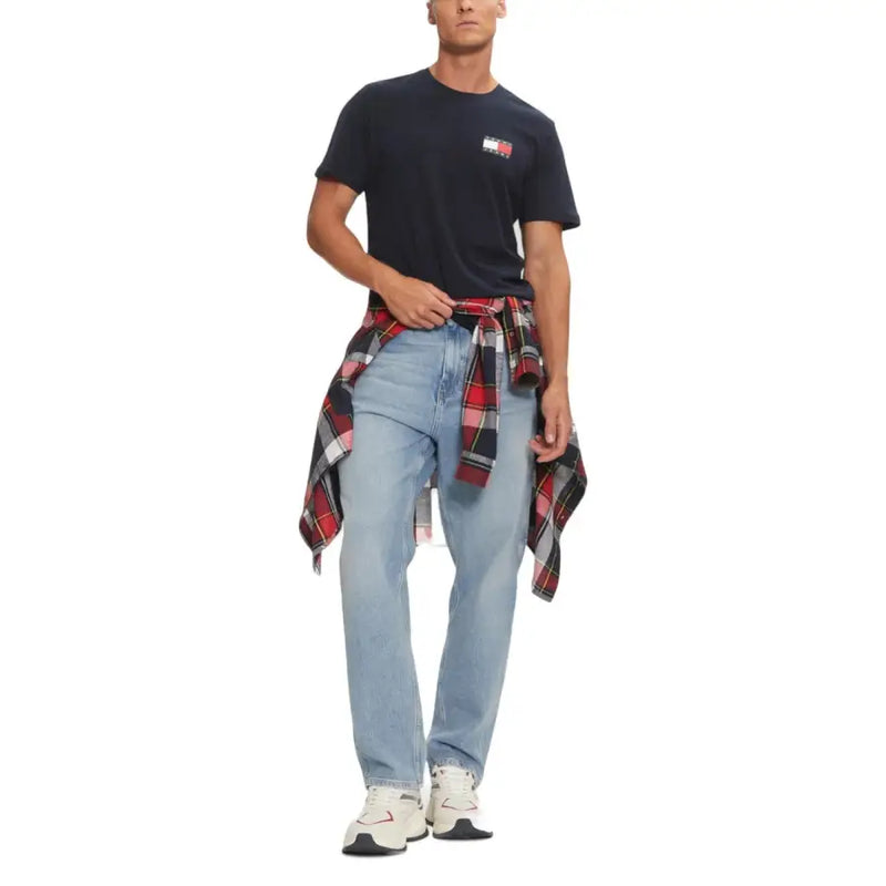 Man wearing navy blue Tommy Hilfiger T-shirt with light blue jeans and plaid shirt tied around waist