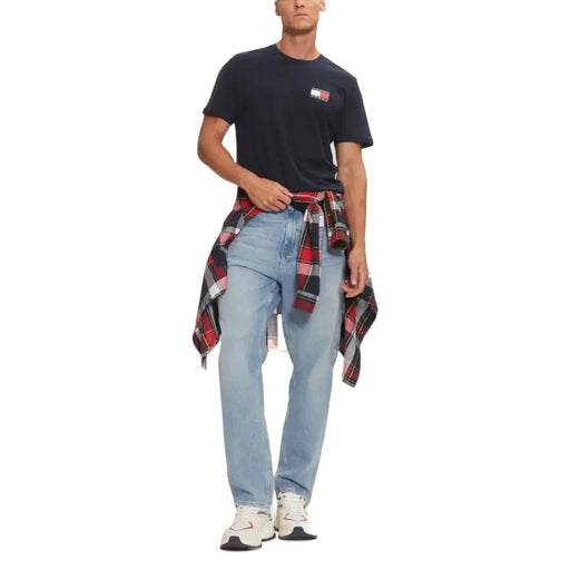 Man wearing navy blue Tommy Hilfiger T-shirt with light blue jeans and plaid shirt tied around waist