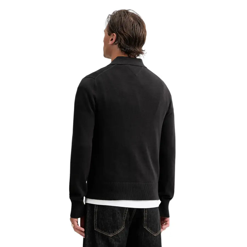 Polo slim noir Tommy Hilfiger Jeans pour homme, pull en maille noire en coton biologique avec poignets et ourlet côtelés, porté sur une chemise blanche