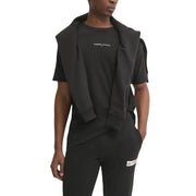Sweat à capuche noir Tommy Hilfiger Jeans porté sur un t-shirt et un pantalon noirs assortis, avec un logo discret en blanc sur la poitrine.