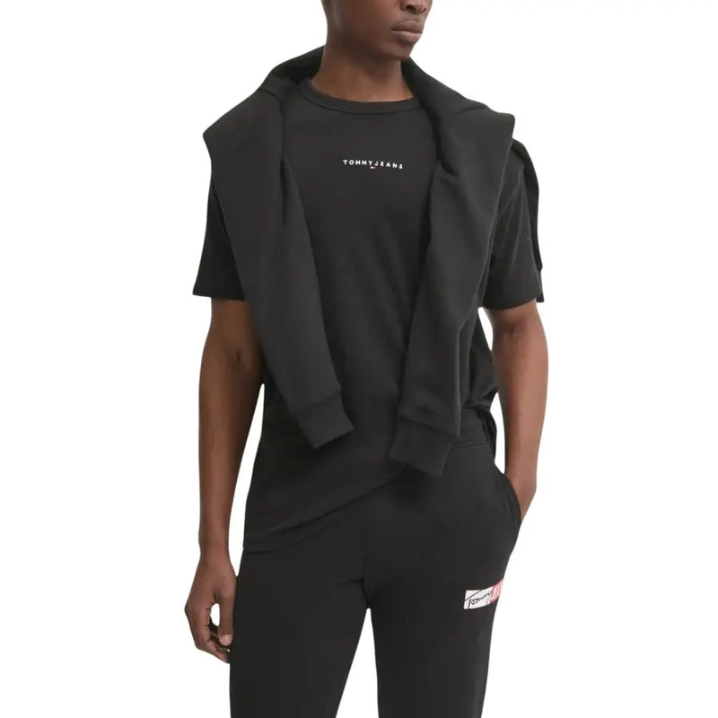 Sweat à capuche noir Tommy Hilfiger Jeans porté sur un t-shirt et un pantalon noirs assortis, avec un logo discret en blanc sur la poitrine.