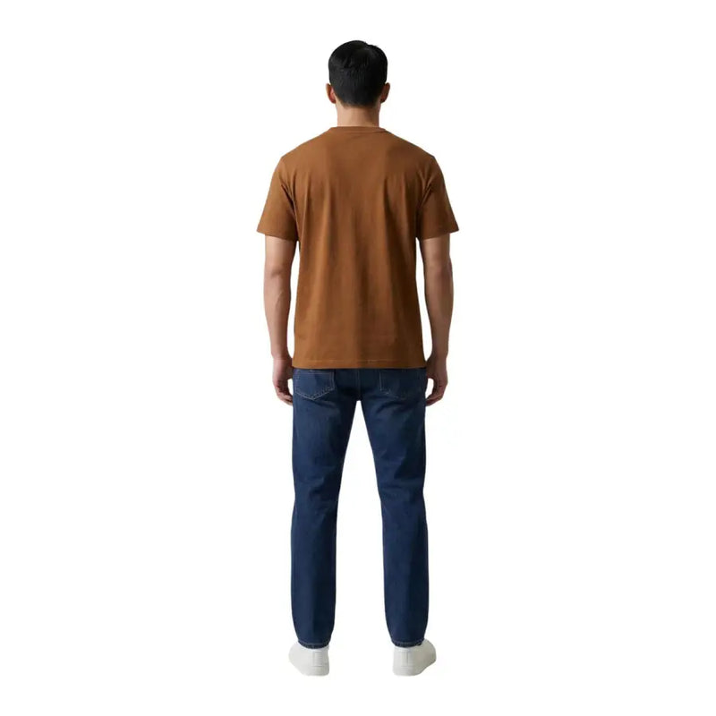Un homme portant un Tommy Hilfiger T-shirt marron en coton à col rond porté avec un jean bleu foncé
