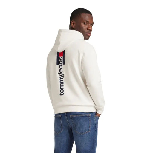 Sweat à capuche Tommy Hilfiger Jeans pour homme, couleur crème, en coton biologique blanc, avec logo noir vertical et bande au dos.