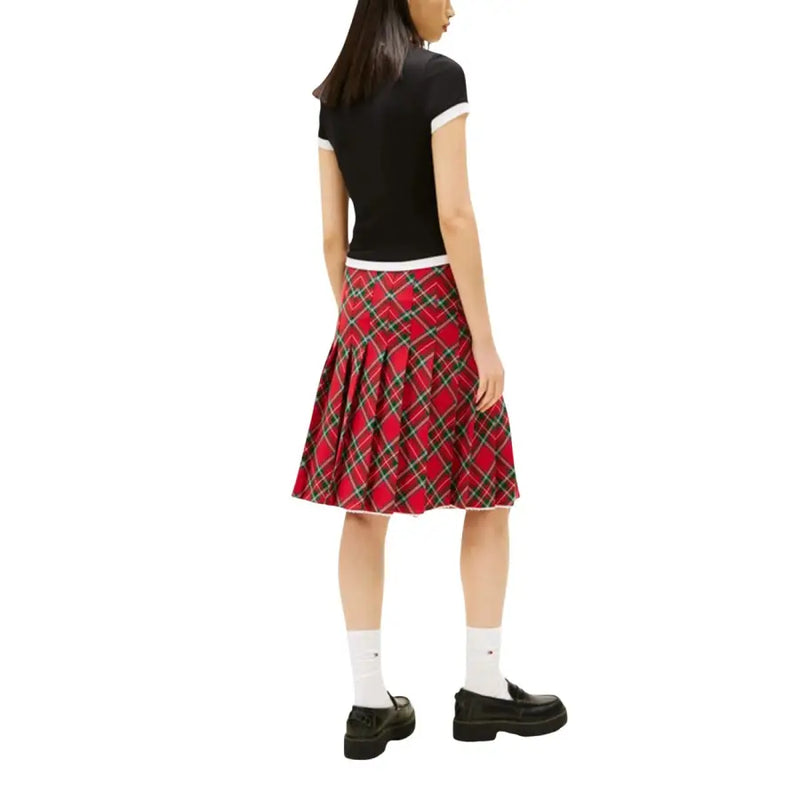 Jupe plissée à carreaux rouges avec des accents noirs et verts, portée avec un jean Tommy Hilfiger noir en coton biologique pour femme t-shirt