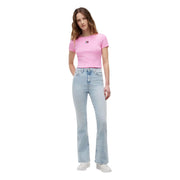 Une femme portant un t-shirt court Tommy Hilfiger en coton côtelé rose, associé à un jean évasé délavé clair.