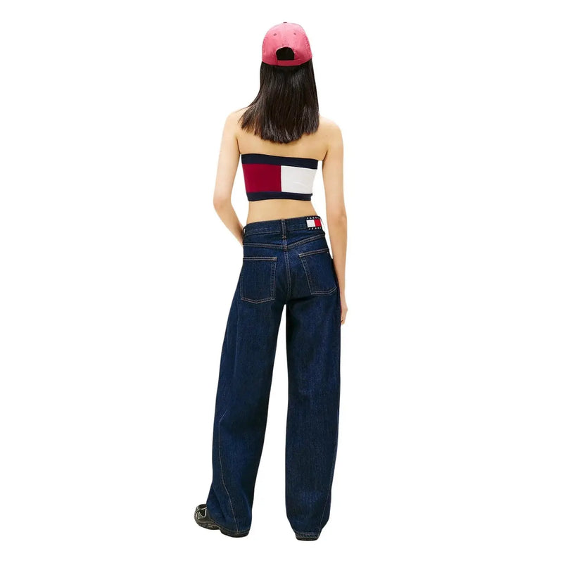 Une femme portant un jean Tommy Hilfiger bleu foncé à jambes larges en coton biologique avec logo à l'arrière de la ceinture et une casquette rose