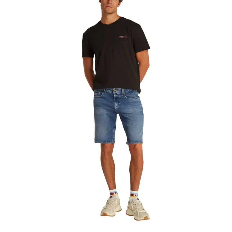 Black t-shirt with white logo, denim shorts, and beige sneakers.