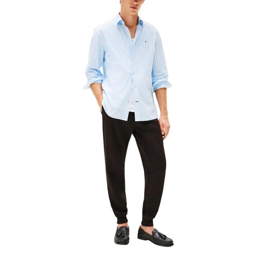 Chemise boutonnée en coton à rayures verticales bleu clair et blanches, manches retroussées, portée avec un pantalon en coton noir Tommy Hilfiger pour homme