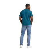 Un homme porte un t-shirt à manches courtes en coton biologique vert turquoise associé à un jean en denim délavé clair. Tommy Hilfiger