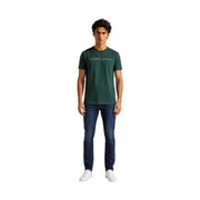 Tommy Hilfiger T-shirt homme vert en coton bio, coupe classique, porté avec un jean Tommy vert foncé et un logo blanc sur la poitrine.