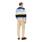 A man wearing a navy light blue and yellow striped rugby sweater paired with Tommy Hilfiger jeans trousers