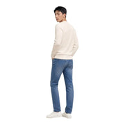 Un homme portant un vêtement couleur crème Tommy Hilfiger Pull blanc à col rond en maille de coton biologique, porté avec un jean bleu