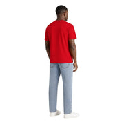 Un homme porte un t-shirt rouge à manches courtes en coton bio Tommy Hilfiger avec un jean délavé.